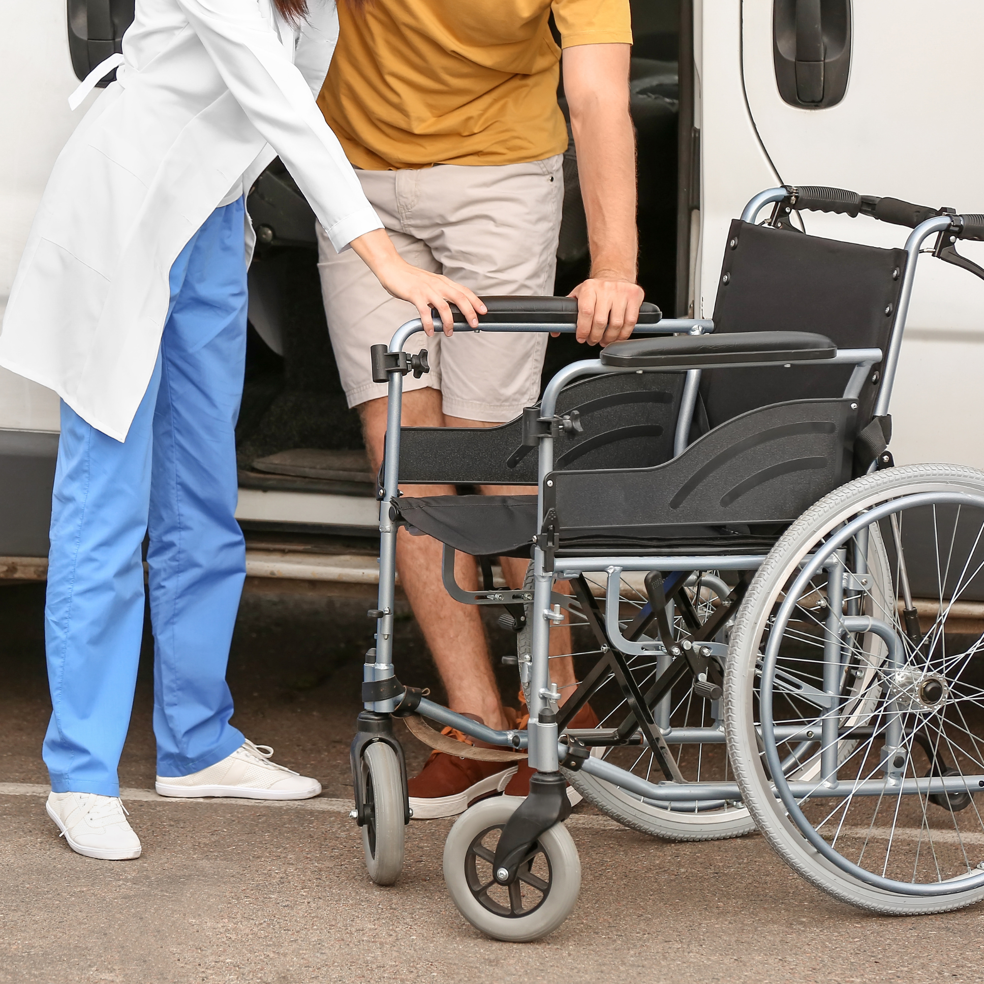 Caregiver assisting a passenger with a wheelchair into a medical transport van